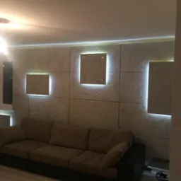 Wykończona ściana z paneli dekoracyjnych z podświetleniem LED, szara sofa w salonie, widok z boku.