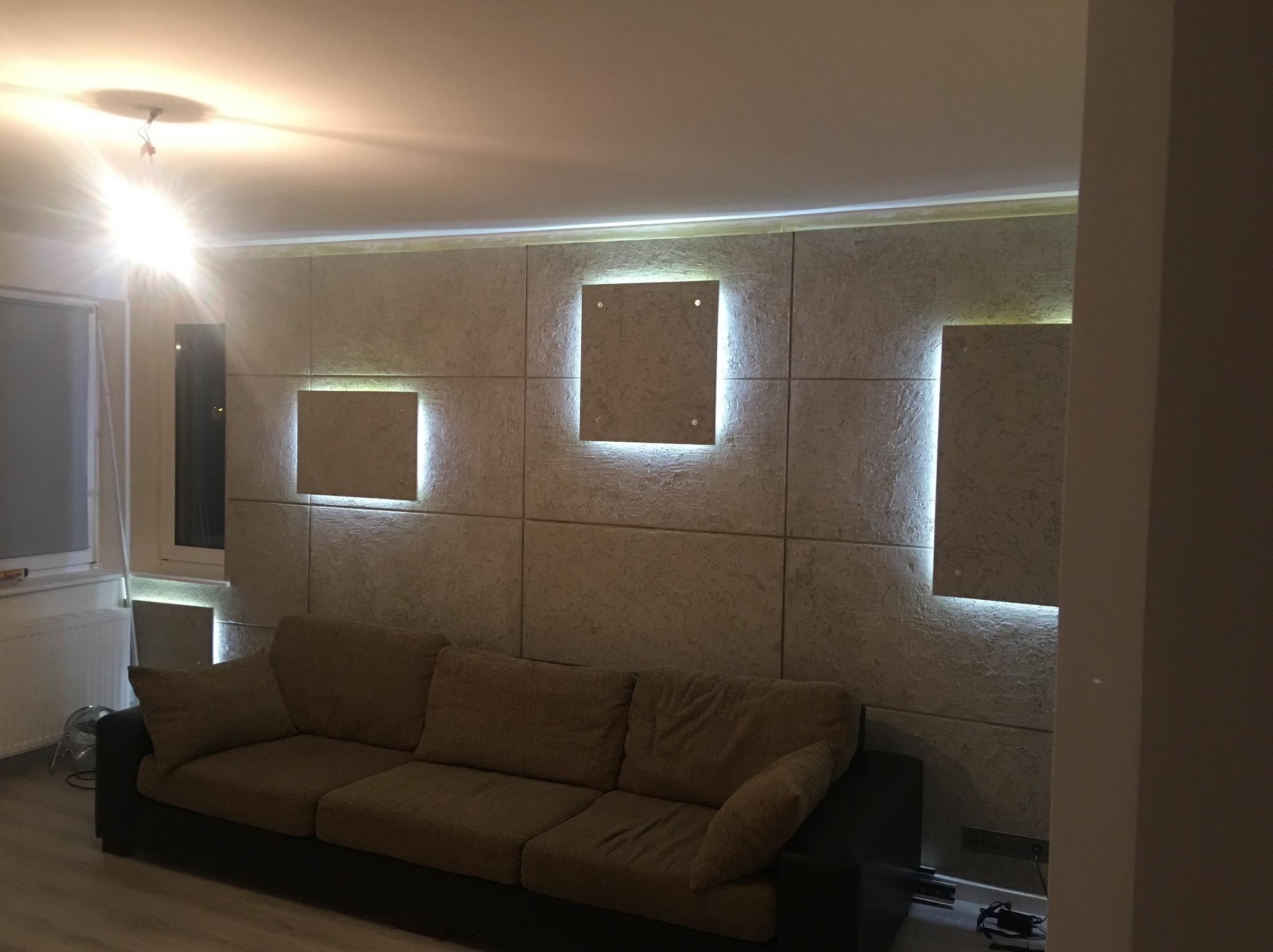 Wykończona ściana z paneli dekoracyjnych z podświetleniem LED, szara sofa w salonie, widok z boku.