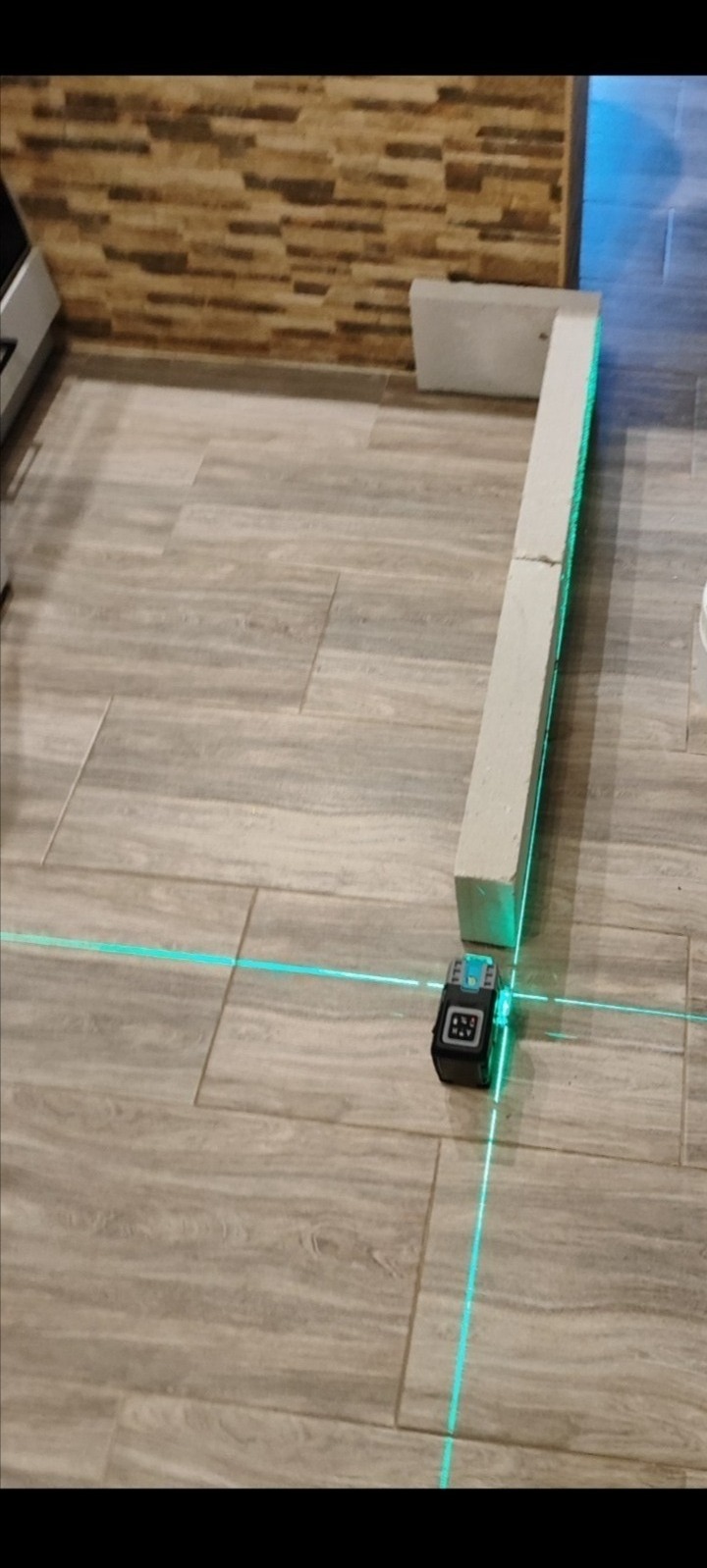 Poziomica laserowa wyznaczająca linię na podłodze z płytek ceramicznych, obok bloczek z betonu komórkowego.