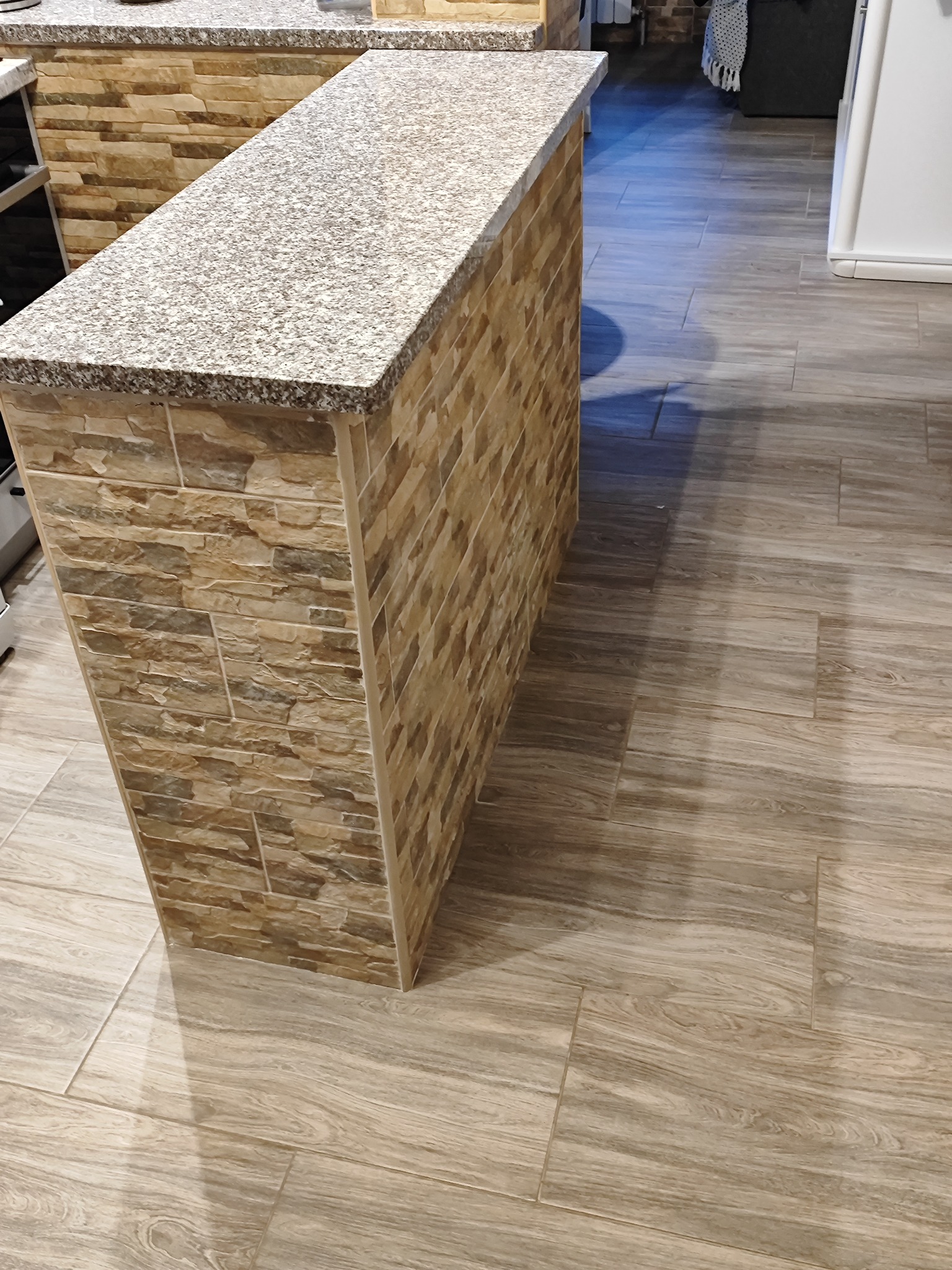 Wykończona wyspa kuchenna z blatem w kolorze soli i pieprzu oraz okładziną z płytek imitujących kamień, dopasowana do podłogi z płytek drewnopodobnych w Ustrzykach Dolnych.