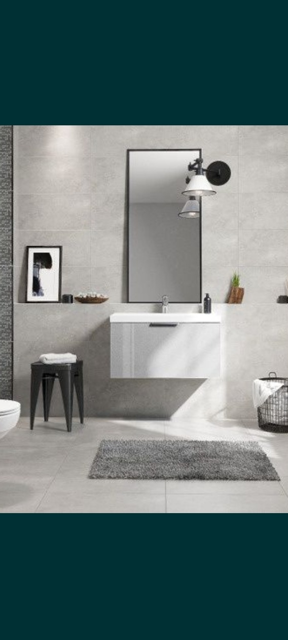 Nowoczesna łazienka z szarymi płytkami, wiszącą szafką z umywalką, lustrem w czarnej ramie, metalowym stołkiem i dywanikiem typu shaggy.