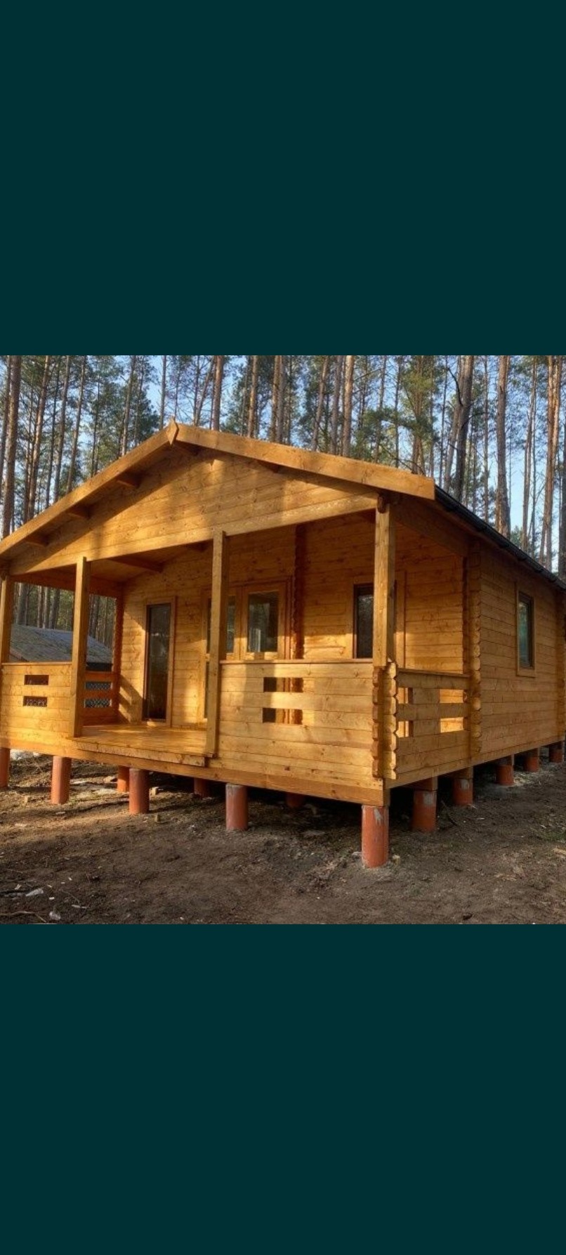 Nowy, drewniany domek letniskowy z gankiem, na fundamencie z betonowych rur, w otoczeniu wysokich sosen.