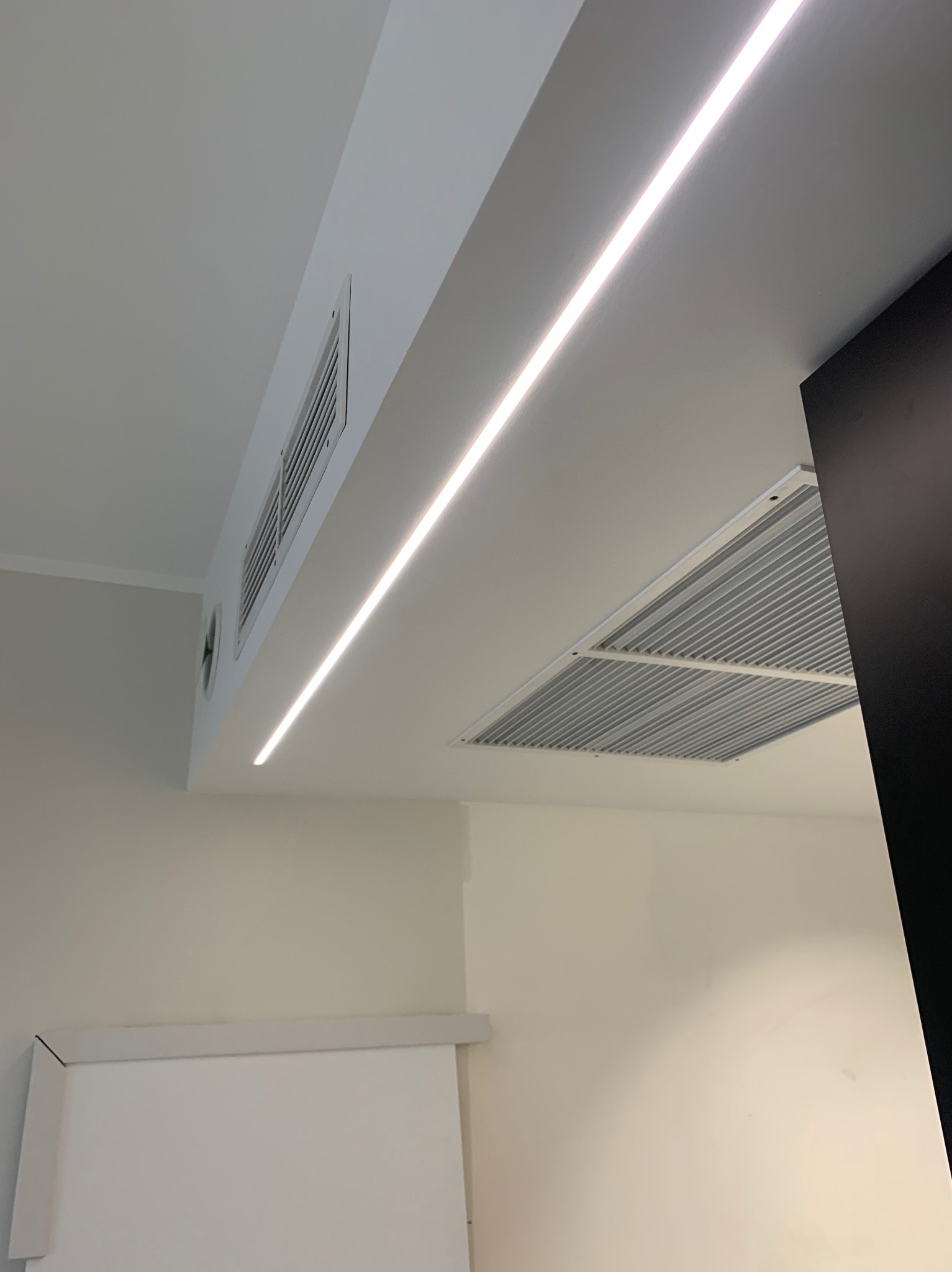 Minimalistyczne wnętrze z podwieszanym sufitem, oświetleniem LED i kratkami wentylacyjnymi.