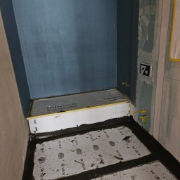 Wiktoria Iwańska Hydro-PUR Solution - Przygotowanie podłoża pod płytki w łazience: hydroizolacja z użyciem maty uszczelniającej Ardex SK 100 W i taśmy uszczelniającej na styku ściany i podłogi, widoczne instalacje wodne i fragment...