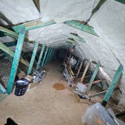Poddasze po ociepleniu pianką PUR: biała izolacja pokrywa skośne ściany i drewnianą konstrukcję dachu. Widoczne narzędzia i materiały budowlane.