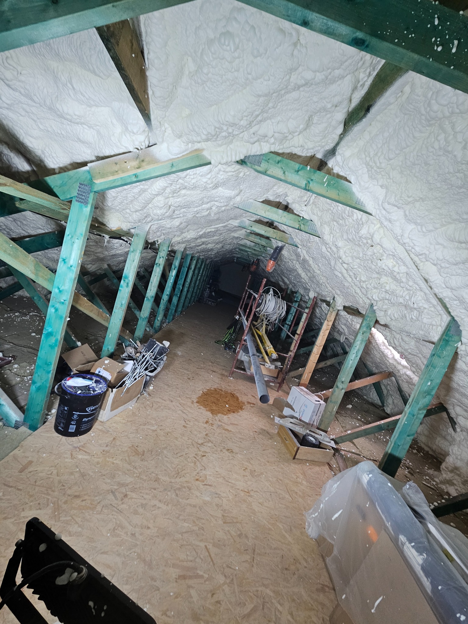 Poddasze po ociepleniu pianką PUR: biała izolacja pokrywa skośne ściany i drewnianą konstrukcję dachu. Widoczne narzędzia i materiały budowlane.