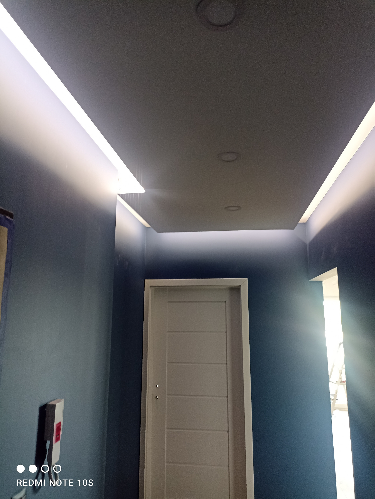 Nowoczesne oświetlenie sufitowe LED w korytarzu z ciemnoniebieskimi ścianami i białą, minimalistyczną stolarką drzwiową.