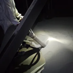 Pracownik w kombinezonie ochronnym usuwa biały pył z powierzchni za pomocą odkurzacza przemysłowego w słabo oświetlonym pomieszczeniu.