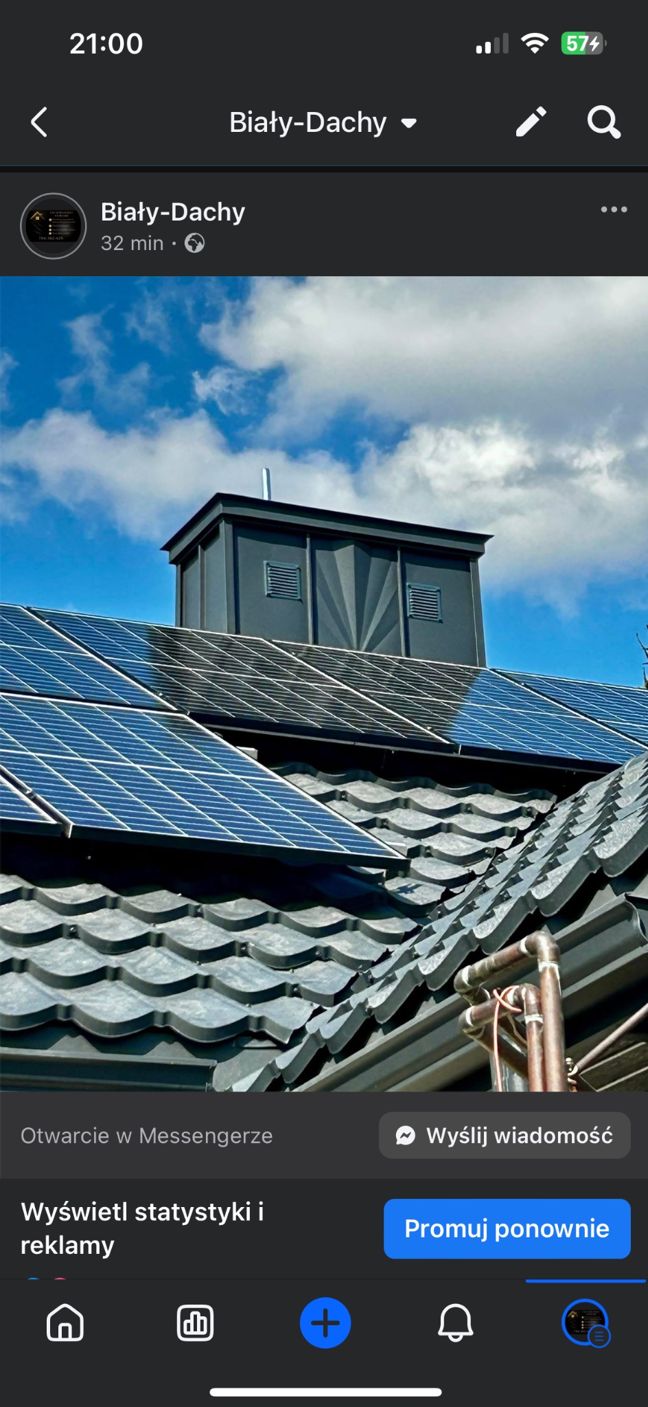 Szary dach z panelami słonecznymi i szarą nadbudówką wentylacyjną na tle błękitnego nieba z chmurami. Widoczne rury na dachu.