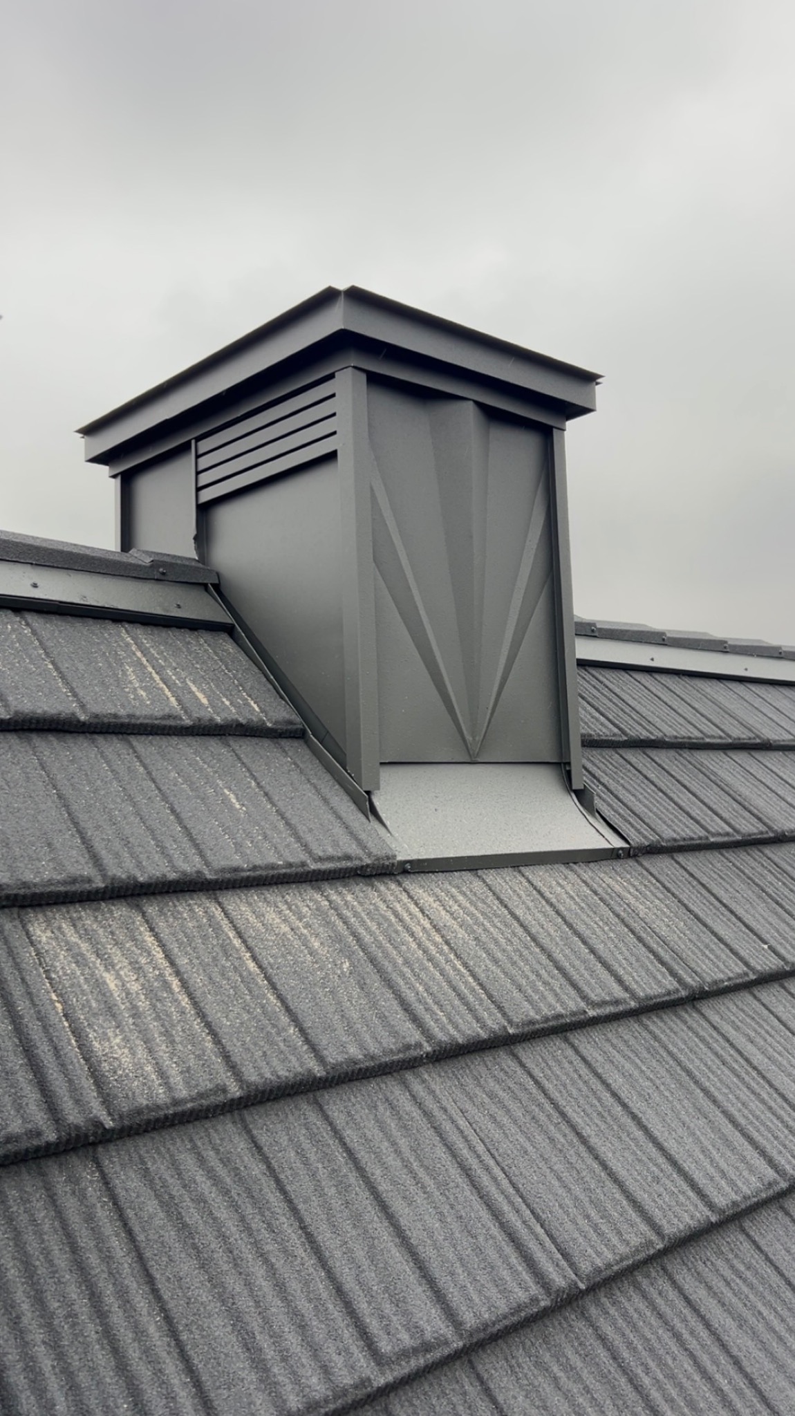 Szary dach z blachy z kominem wentylacyjnym o geometrycznym wzorze w kształcie litery V. Nowoczesne pokrycie dachowe w pochmurny dzień.