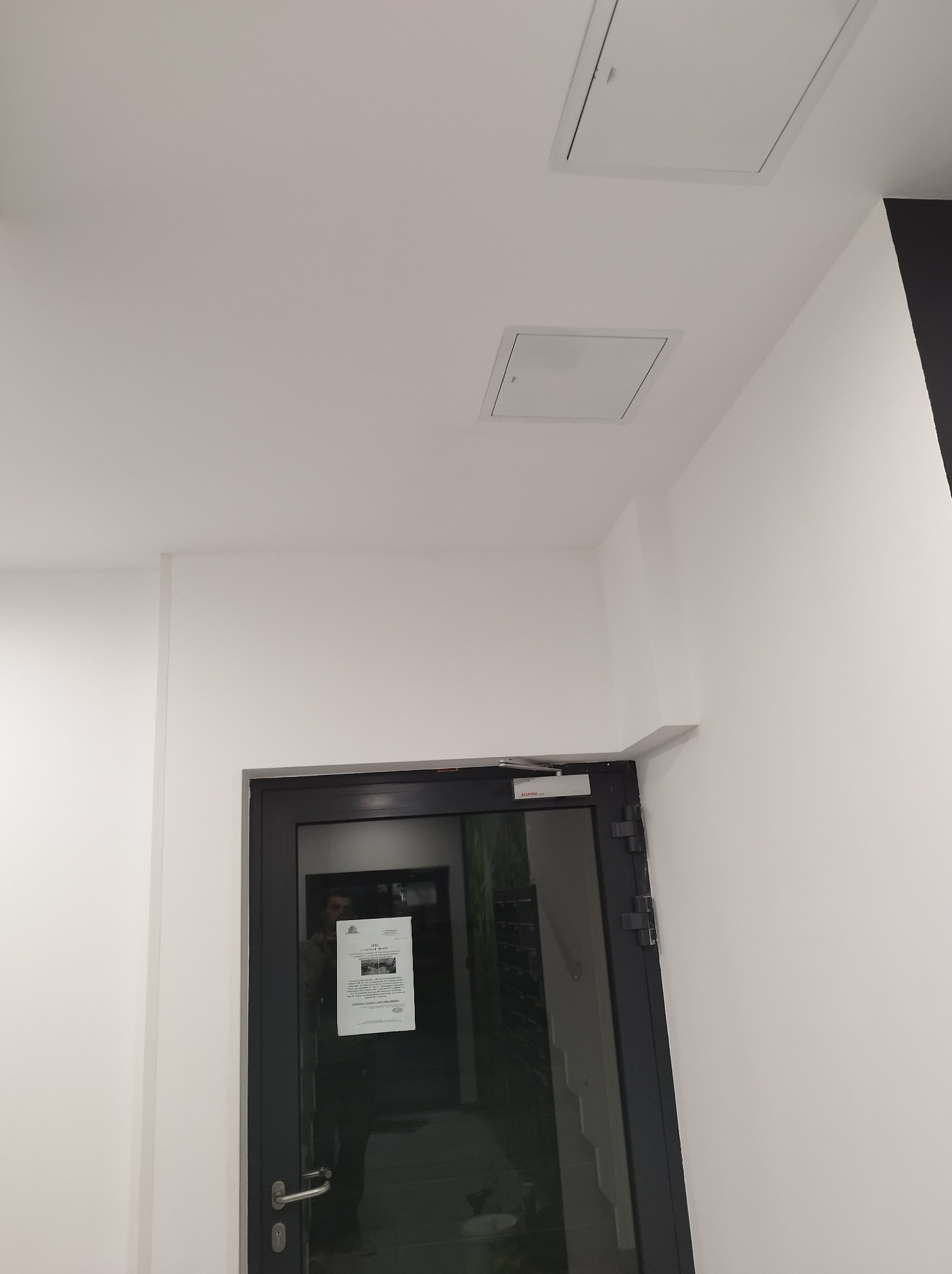 Białe wnętrze z zamontowanymi drzwiami z czarną ramą i dwoma włazami rewizyjnymi w suficie.