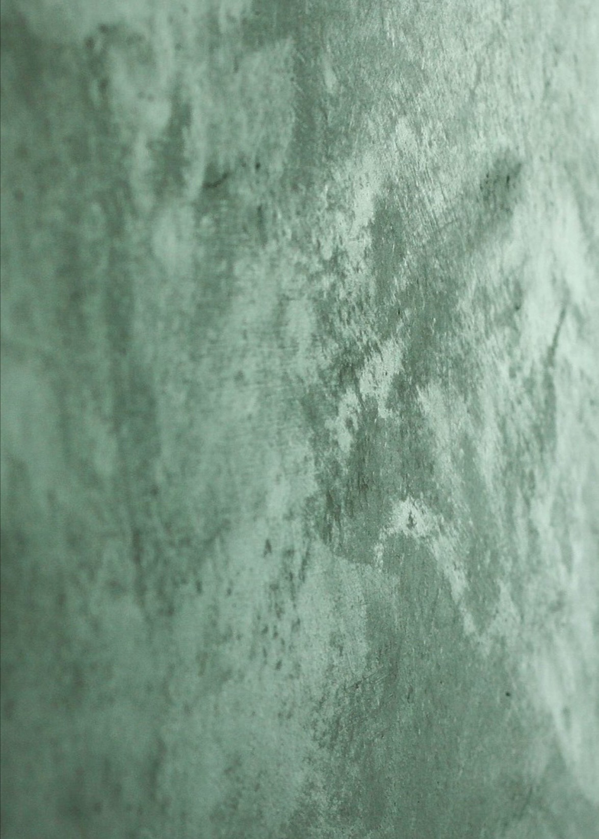 Zielona ściana z efektem dekoracyjnej, nierównej faktury, imitującej surowy beton, sfotografowana pod kątem.