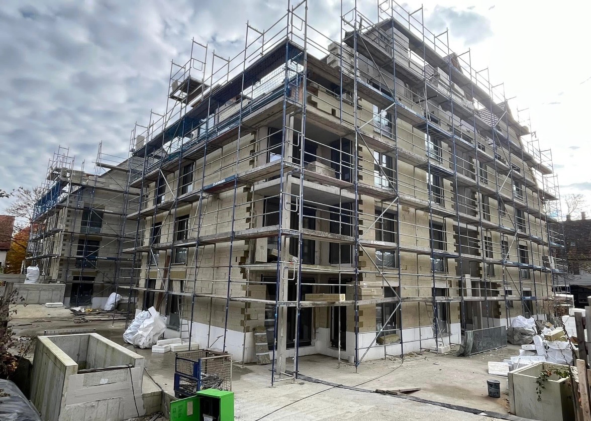 Budynek wielorodzinny w trakcie prac wykończeniowych, z widocznymi rusztowaniami, oknami i częściowo ocieplonymi ścianami.