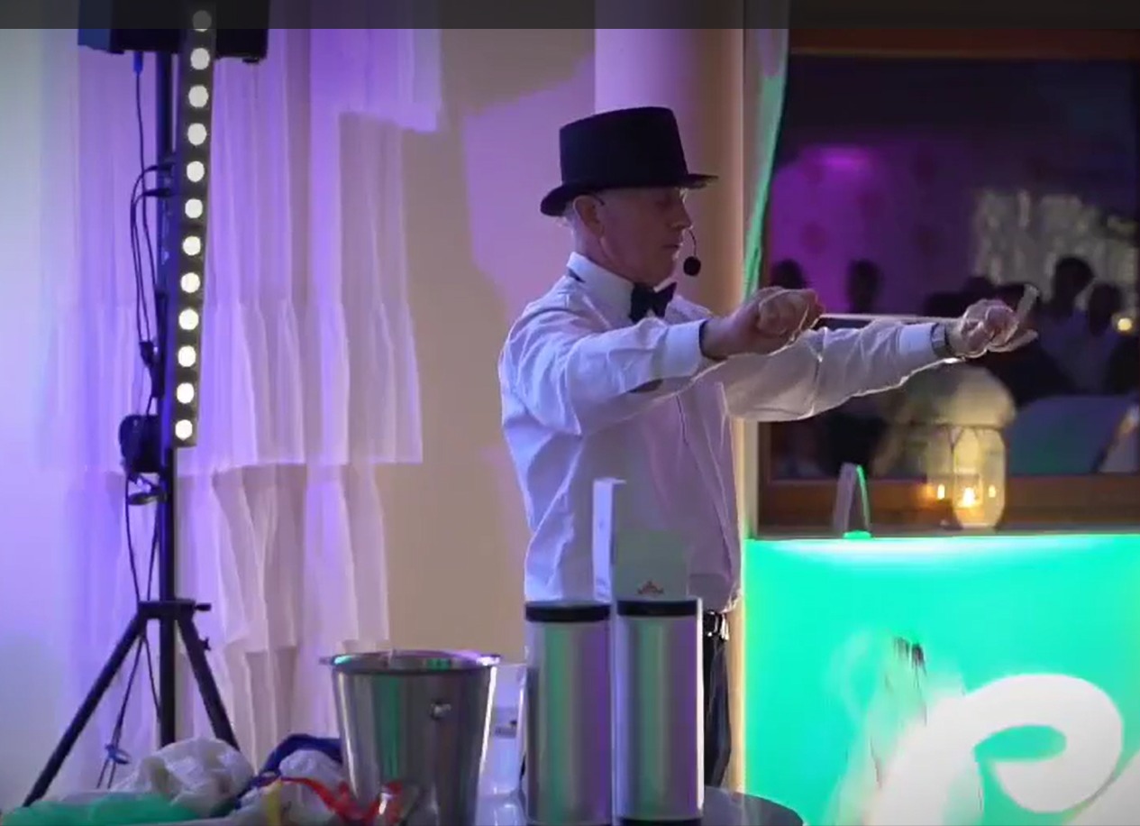 Iluzjonista w cylindrze prezentuje trik z kartami na tle dekoracji świetlnych i zasłon podczas występu na imprezie.