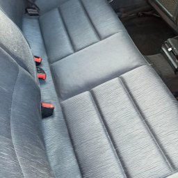 Picuś - Szare, materiałowe siedzenie samochodowe z trzema zagłówkami i pasami bezpieczeństwa, widoczne ślady użytkowania.