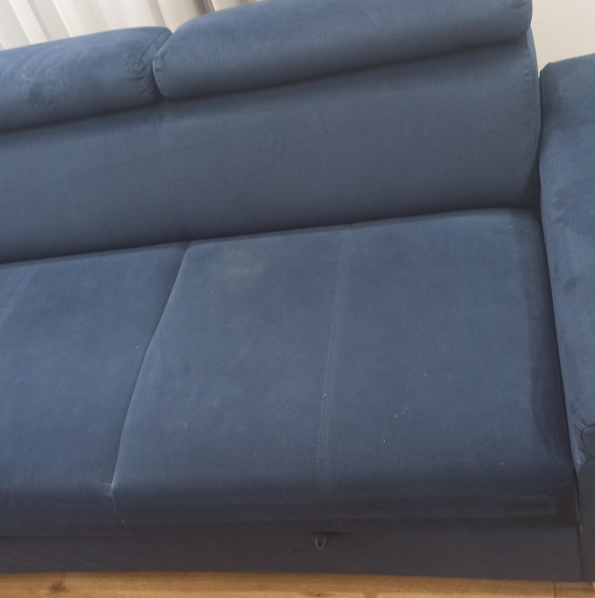 Fragment narożnika w odcieniach granatu na drewnianej podłodze, widoczne delikatne zabrudzenia na siedzisku.