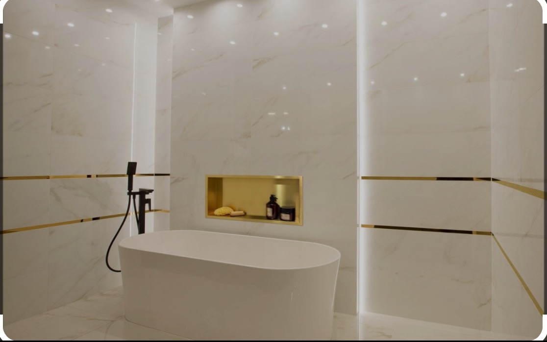 Nowoczesna łazienka z białą wanną wolnostojącą, czarną armaturą i płytkami imitującymi marmur z złotymi akcentami oraz wnęką z akcesoriami.