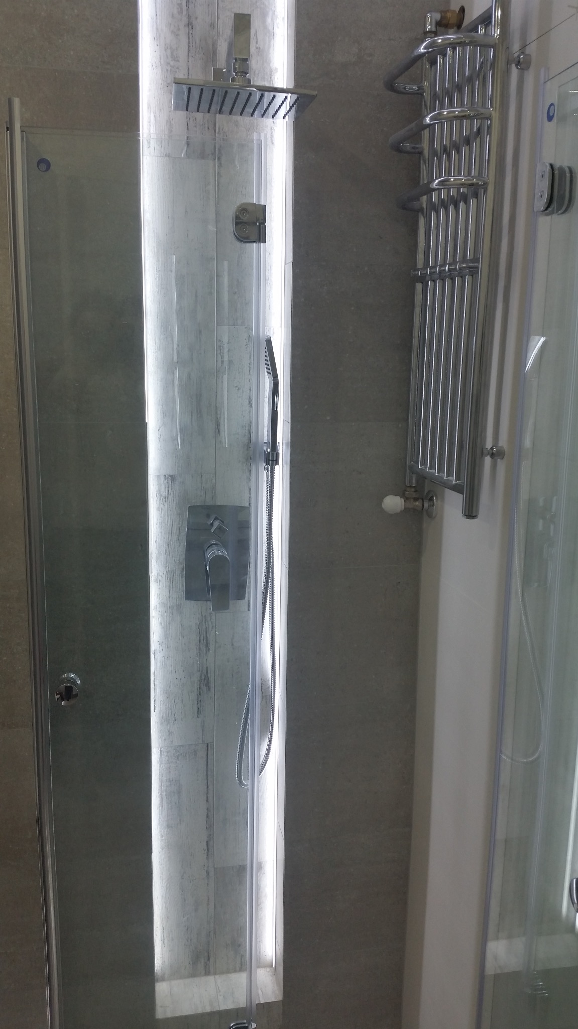 Nowoczesna kabina prysznicowa z deszczownicą i panelem sterującym w szarej łazience z grzejnikiem drabinkowym.