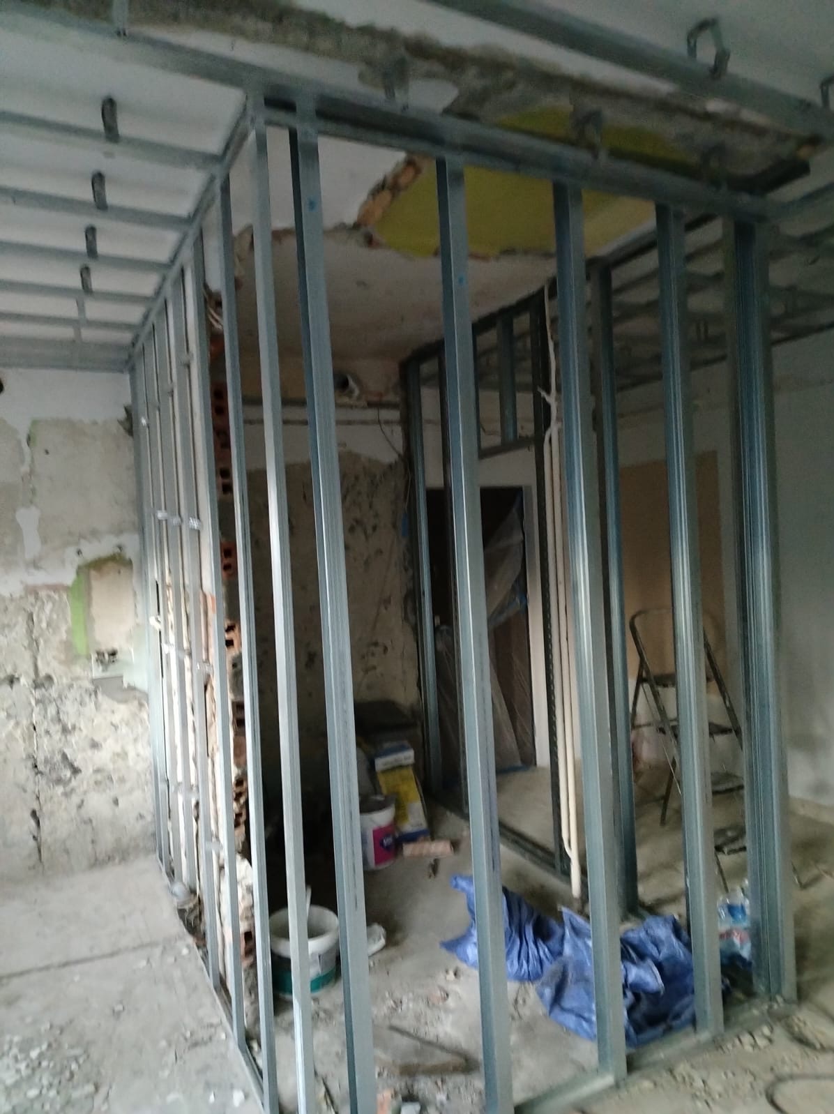 Konstrukcja ścianki działowej z profili stalowych w surowym wnętrzu, widoczne ślady po starych instalacjach, farbach i tynkach, przygotowanie do dalszych prac wykończeniowych.