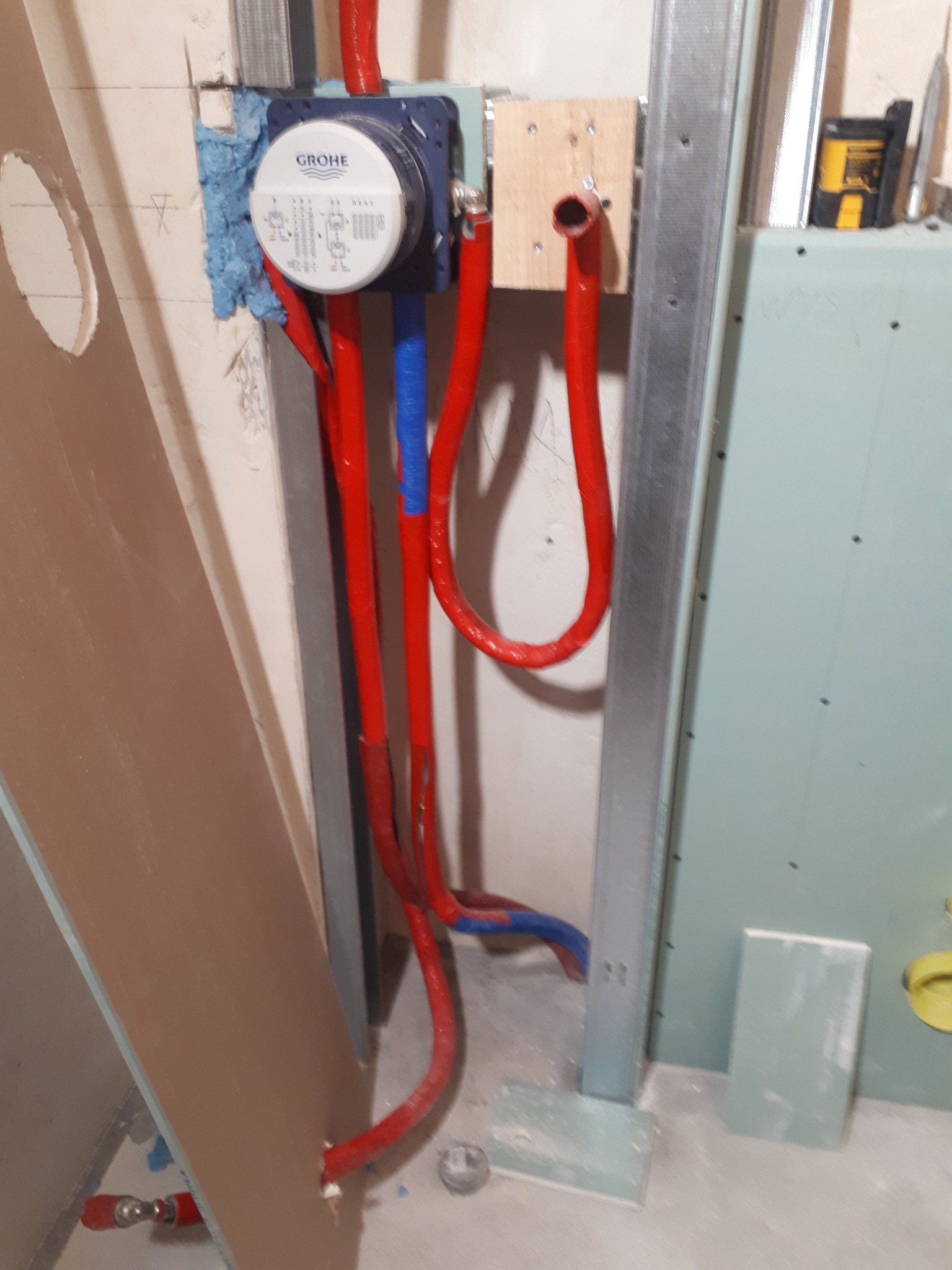 Montaż podtynkowego zestawu prysznicowego Grohe z czerwonymi i niebieskimi rurami doprowadzającymi wodę, osadzony w ścianie z płyt kartonowo-gipsowych na metalowym stelażu, zabezpieczony pianką...