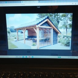 Grzegorz Karbowiak - Zdjęcie przedstawia oszkloną altanę z drewnianą konstrukcją i czarnymi elementami wykończeniowymi, widoczną na ekranie laptopa. Wewnątrz altany znajdują się meble wypoczynkowe. Na zewnątrz widać...