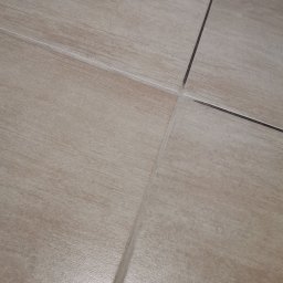 MT Pomoc Sprzątająca - Beżowe płytki podłogowe z ciemniejszymi fugami układające się w regularny wzór, widoczne lekkie zabrudzenia przy fugach.