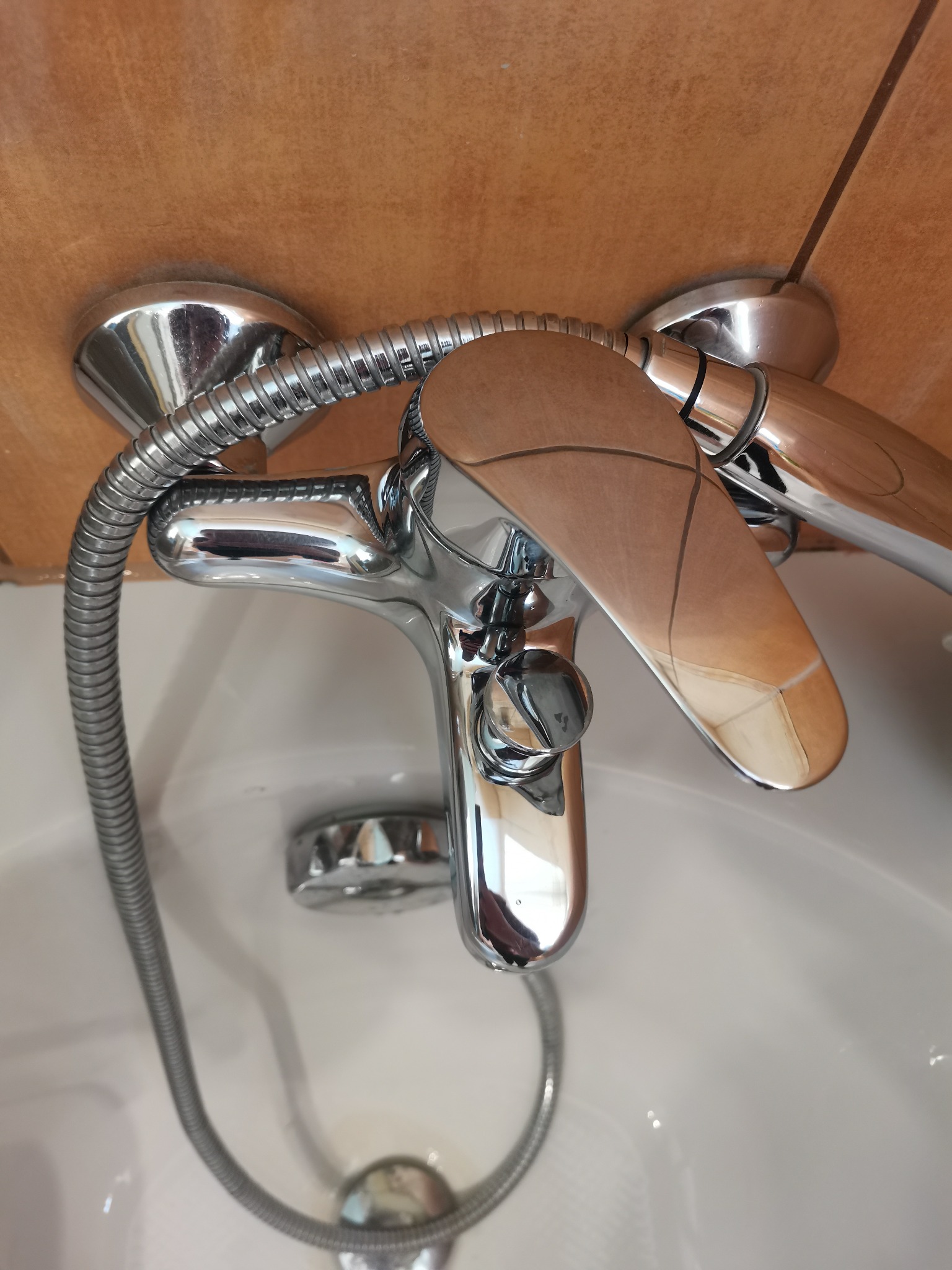 Bateria wannowa chromowana z drewnianą dźwignią mieszacza, zamontowana na brązowych płytkach, widoczna wewnątrz białej wanny.