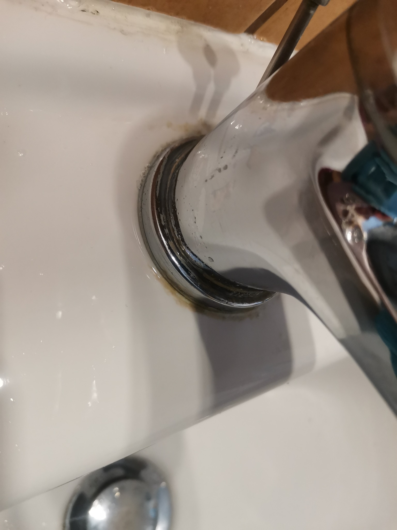 Zacieki i osad wokół chromowanej baterii umywalkowej na białej ceramice.