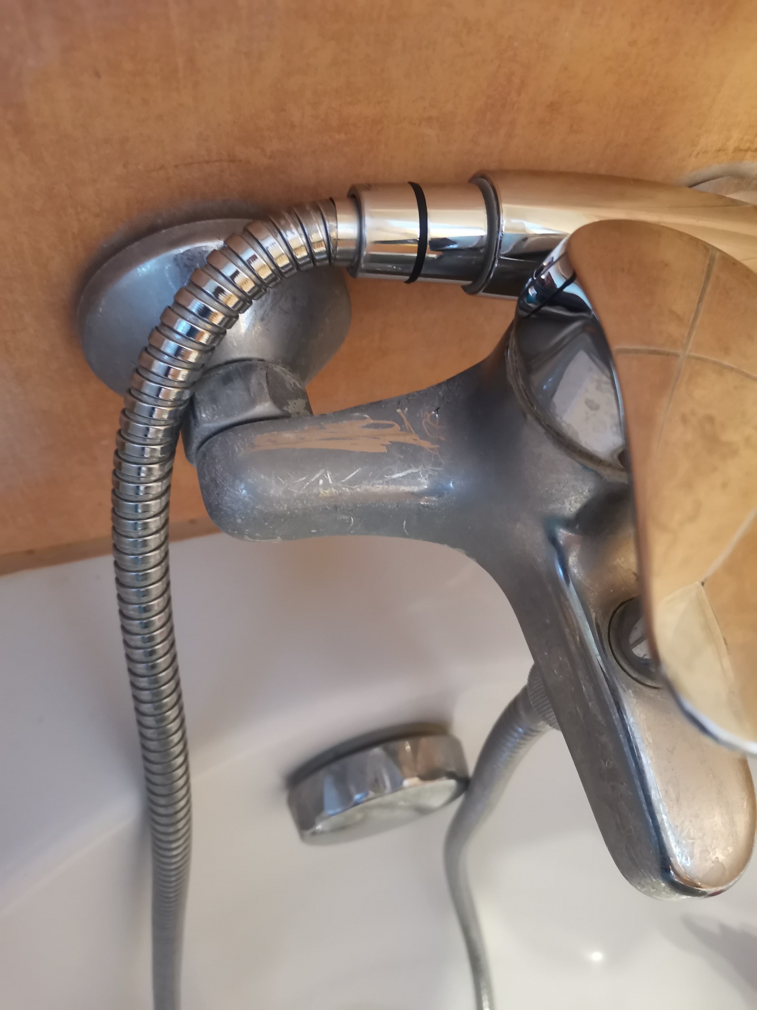 Bateria prysznicowa z widocznymi śladami użytkowania i osadami, zamontowana przy brązowej ścianie wyłożonej płytkami.