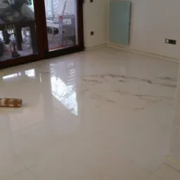 Błyszcząca, kremowa podłoga z płytek imitujących marmur w pustym pokoju z dużym oknem balkonowym i grzejnikiem ściennym.