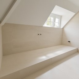 HOME INVESTING Aleksander Zera - Jasna łazienka na poddaszu z beżowymi płytkami, widoczne dwa punkty mocowania baterii i okno dachowe. Minimalistyczny design, czyste linie i neutralna kolorystyka.