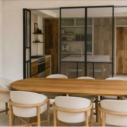 HOME INVESTING Aleksander Zera - Nowoczesna jadalnia z drewnianym stołem i krzesłami w odcieniach beżu, oddzielona szklaną ścianą od kuchni z drewnianą zabudową. Na ścianie abstrakcyjny obraz.