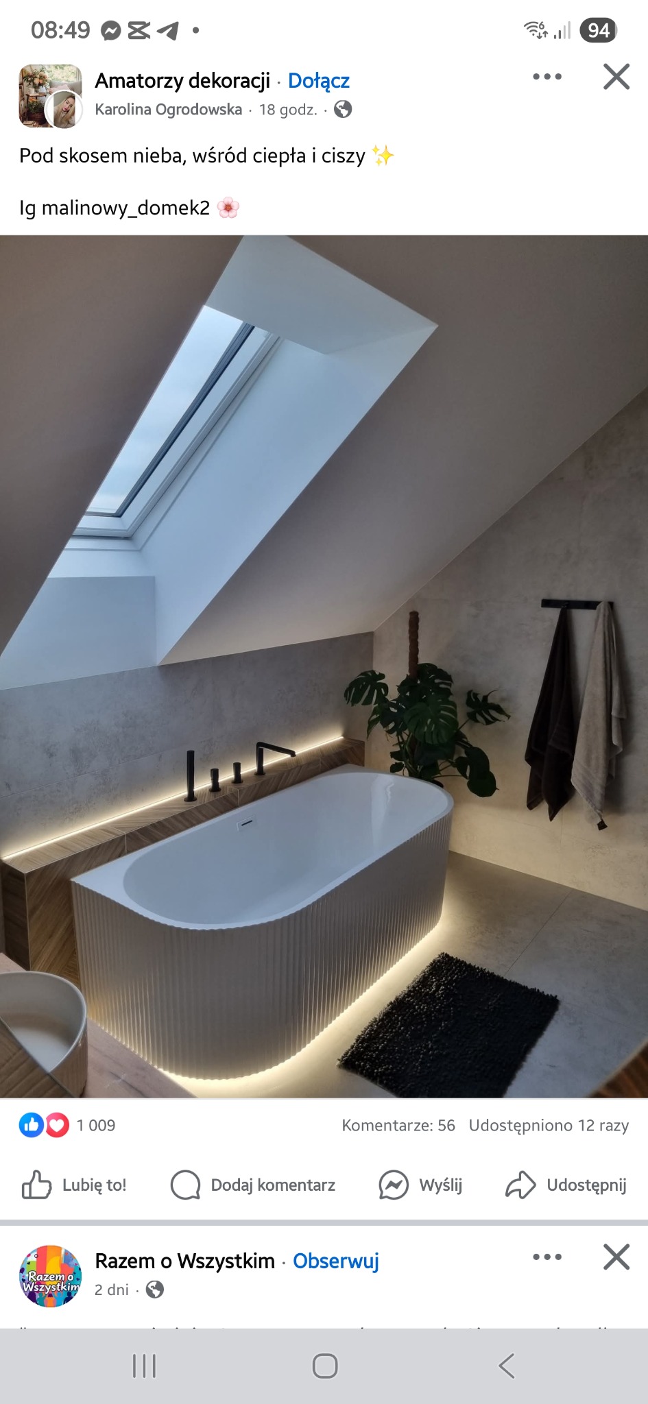 Nowoczesna łazienka na poddaszu z oknem dachowym. Wolnostojąca wanna z podświetleniem LED, szare ściany, roślina doniczkowa i czarny dywanik. Minimalistyczny design.