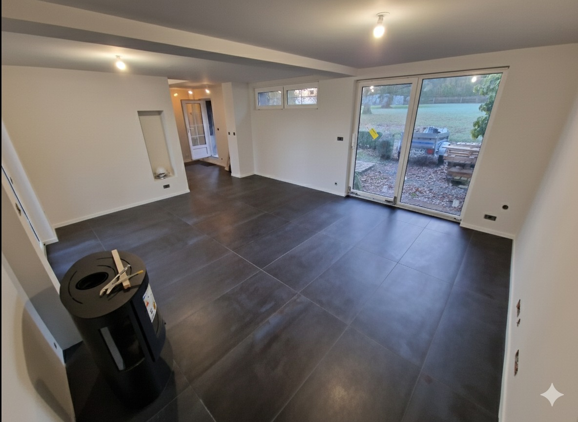 Nowoczesne, ciemne płytki podłogowe w przestronnym, jasnym wnętrzu z dużym oknem i widokiem na zewnątrz. W tle widoczne drzwi i białe ściany.