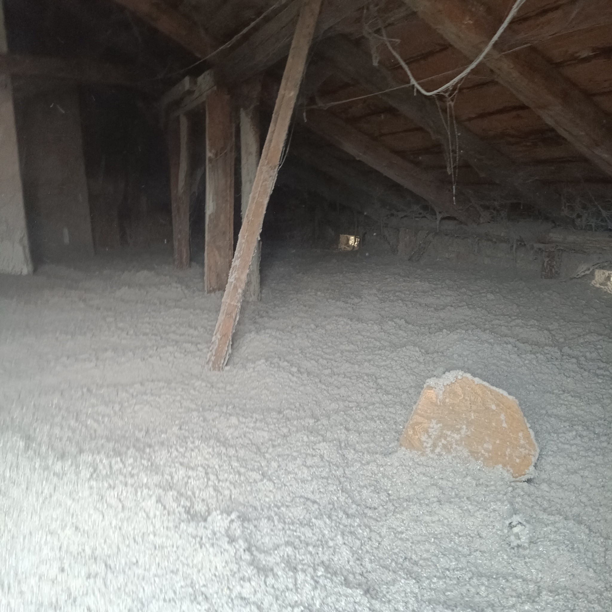 Poddasze po ociepleniu, widoczne drewniane elementy konstrukcyjne i warstwa izolacji z wełny mineralnej, z fragmentem deski na wierzchu izolacji.