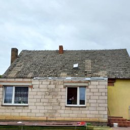 Jgk-Dach Jakub Grześkowiak - Dom w trakcie budowy z widocznym dachem pokrytym starą dachówką. Część elewacji w surowym stanie, druga pomalowana na żółto. Widoczne materiały budowlane.