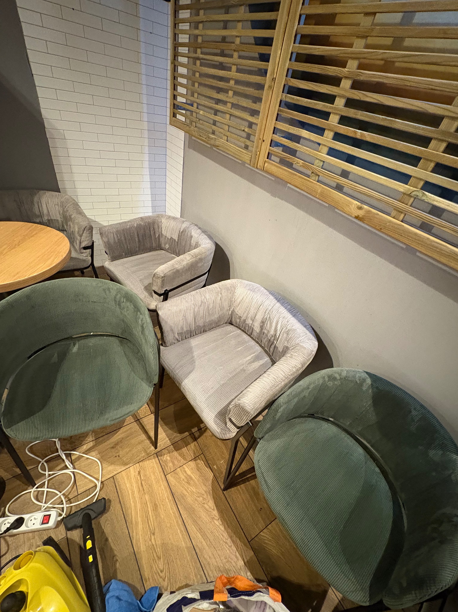 Krzesła tapicerowane w lokalu z widocznym sprzętem do czyszczenia, sugerujące usługę prania tapicerki. Parkiet na podłodze, drewniana przesłona w tle.