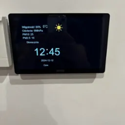Panel sterowania inteligentnego domu w Wieliczce, wyświetlający dane o wilgotności, ciśnieniu, jakości powietrza (PM10, PM2.5) oraz prognozę pogody (słonecznie), z aktualną godziną i datą.