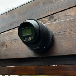 Czarna kamera monitoringu wizyjnego marki Dahua, zamontowana na ścianie z ciemnego, bejcowanego drewna, skierowana w dół.