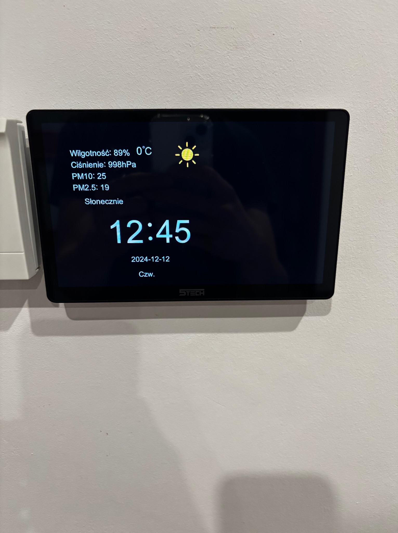 Panel sterowania inteligentnego domu w Wieliczce, wyświetlający dane o wilgotności, ciśnieniu, jakości powietrza (PM10, PM2.5) oraz prognozę pogody (słonecznie), z aktualną godziną i datą.