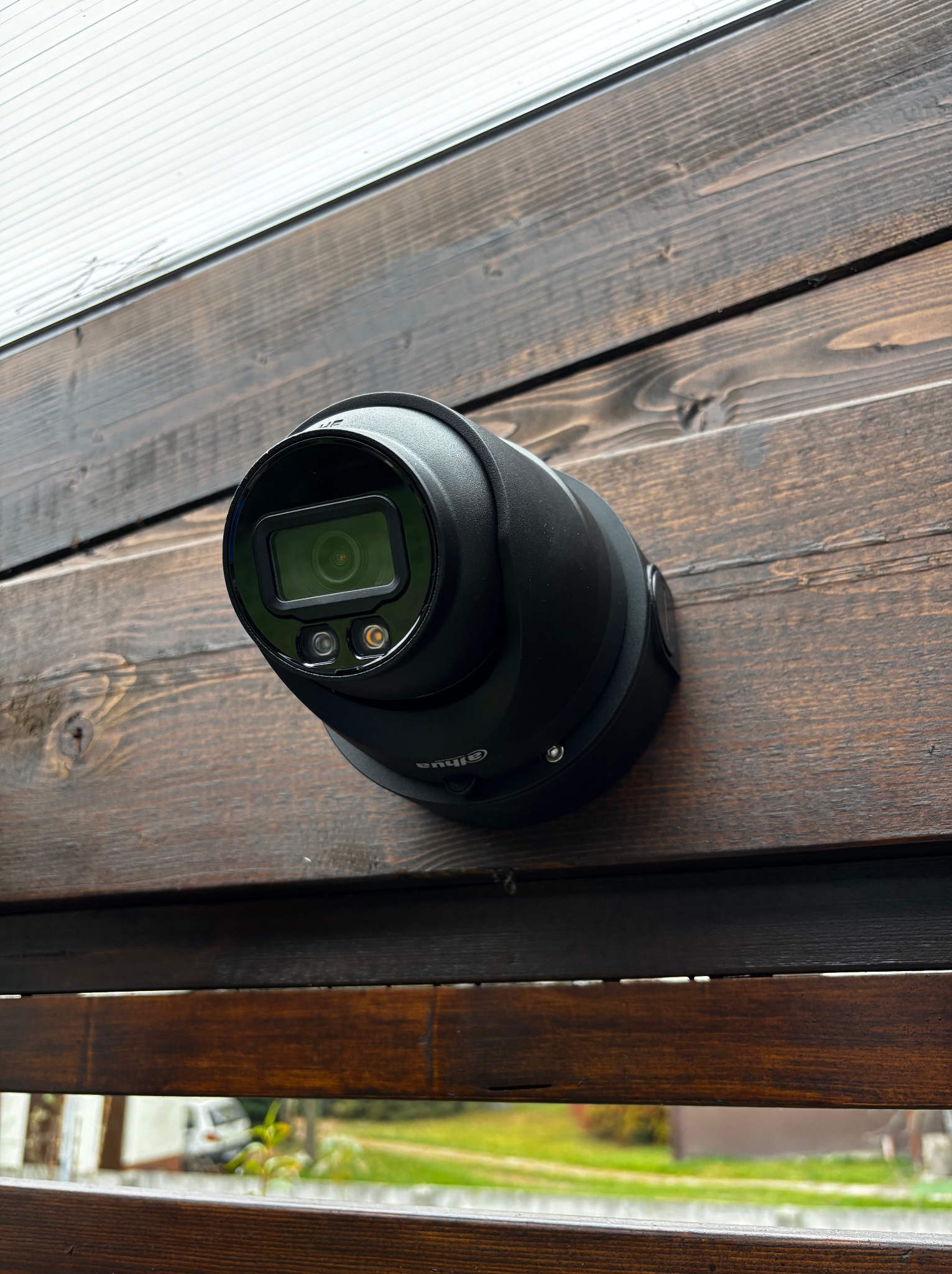 Czarna kamera monitoringu wizyjnego marki Dahua, zamontowana na ścianie z ciemnego, bejcowanego drewna, skierowana w dół.