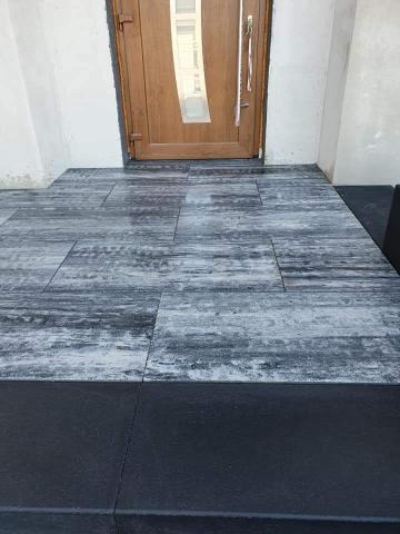 Ułożona kostka brukowa w odcieniach szarości przed wejściem do domu z drewnianymi drzwiami.