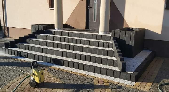 Schody wejściowe do domu wyłożone kostką brukową w odcieniach szarości i czerni, czyszczone myjką ciśnieniową, z widoczną kostką wokół schodów.
