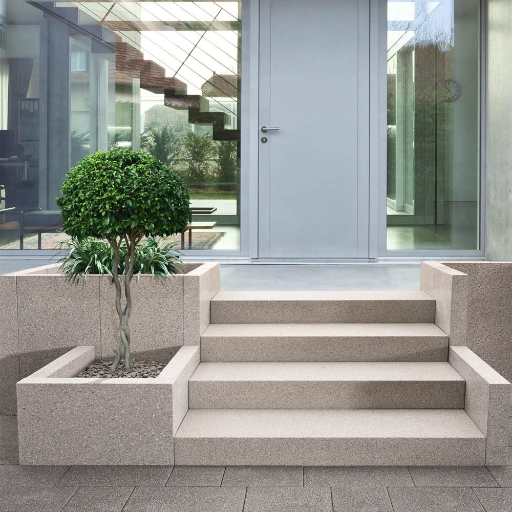 Wejście do domu z czterema stopniami z jasnego, ziarnistego kamienia, obok donica z kulistym drzewkiem; widoczne szare drzwi z przeszkleniami i schody wewnątrz budynku.
