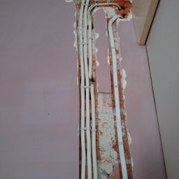 Marcin Włodarczyk Diagnosis - Białe przewody elektryczne prowadzone w bruździe w ceglanej ścianie, zabezpieczone uchwytami, widoczne podczas remontu w Kobyłce.