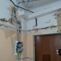 Marcin Włodarczyk Diagnosis - Odsłonięte przewody elektryczne w ścianie podczas remontu, widoczna skrzynka z bezpiecznikami i częściowo usunięty tynk.
