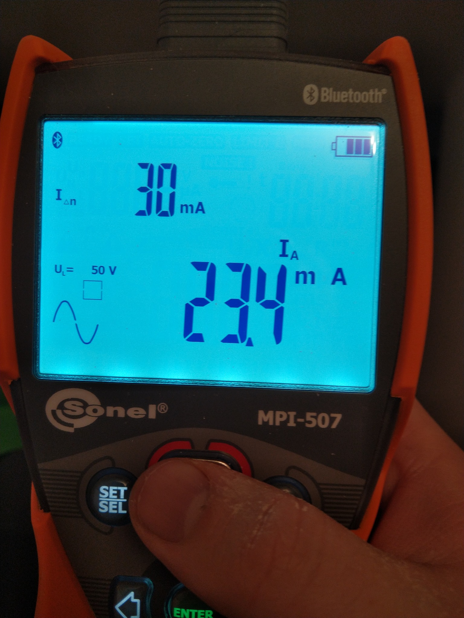 Miernik elektryczny Sonel MPI-507 z podświetlonym ekranem wskazującym wartości 30 mA i 23.4 mA, obsługiwany palcem na przycisku 'SET/SEL'.