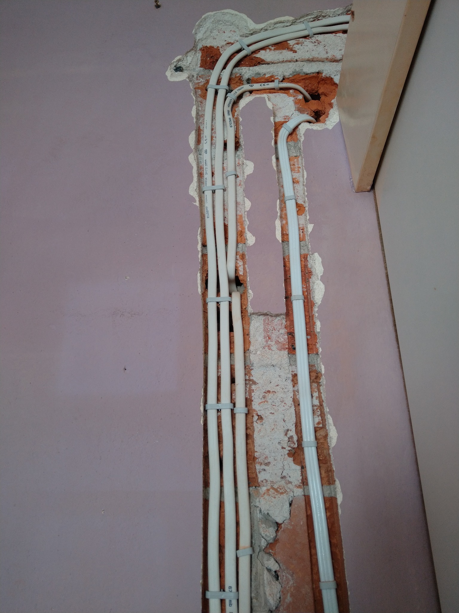 Białe przewody elektryczne prowadzone w bruździe w ceglanej ścianie, zabezpieczone uchwytami, widoczne podczas remontu w Kobyłce.