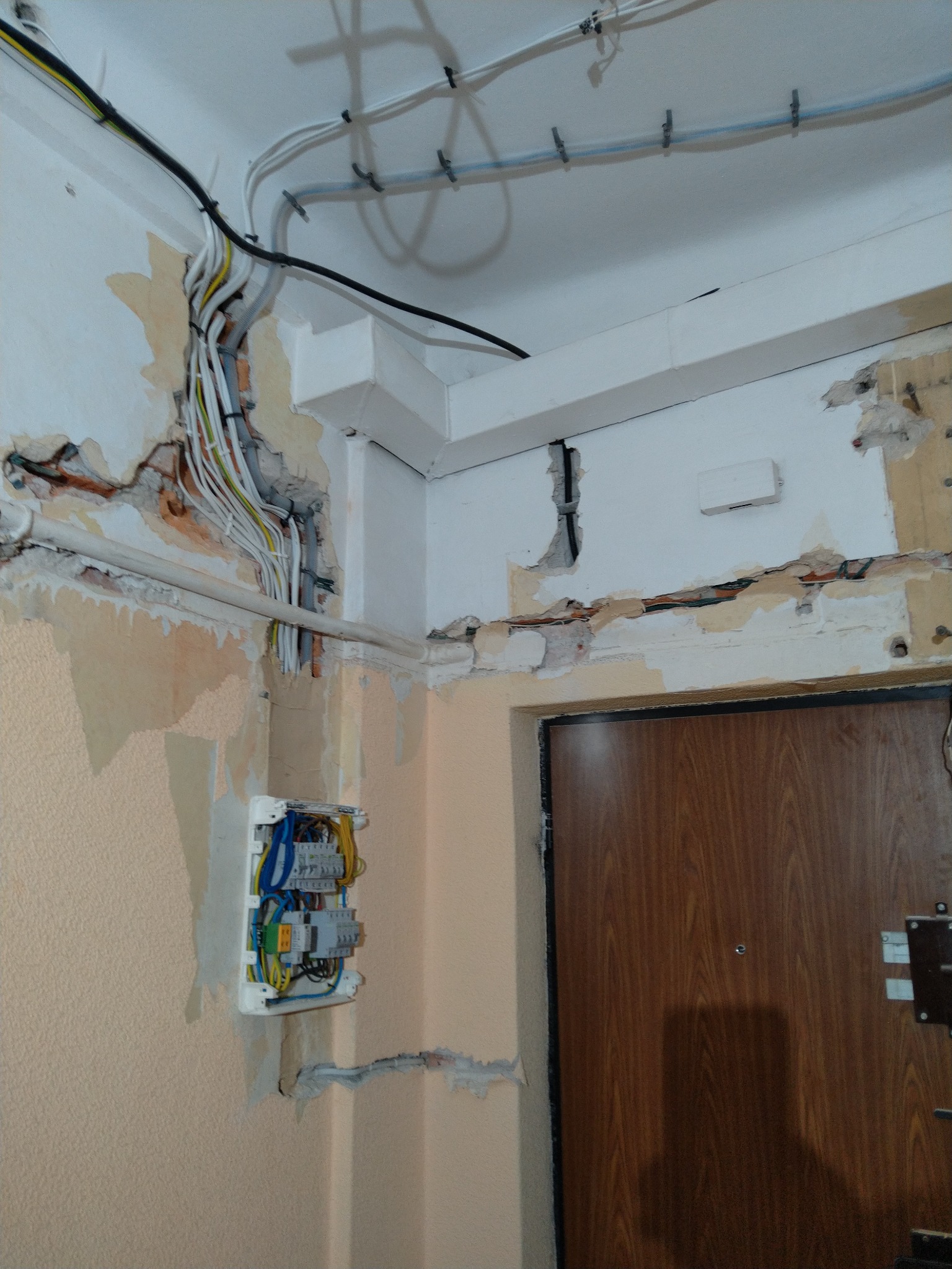 Odsłonięte przewody elektryczne w ścianie podczas remontu, widoczna skrzynka z bezpiecznikami i częściowo usunięty tynk.