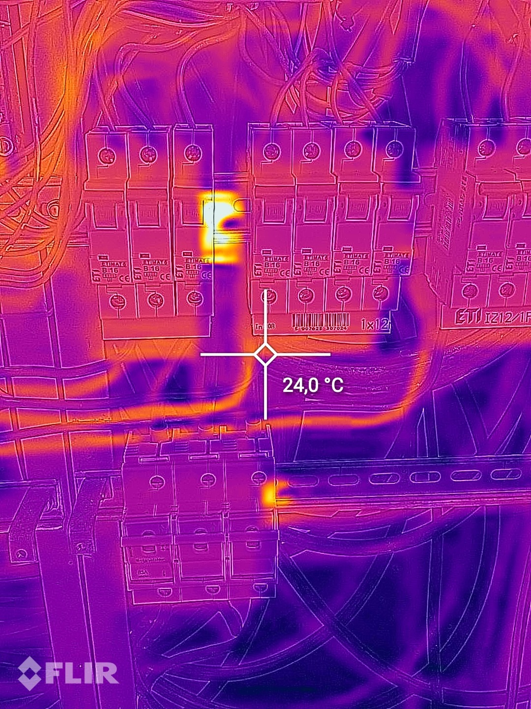 Termowizyjne zdjęcie rozdzielnicy elektrycznej z widocznymi bezpiecznikami, wskazujące na podwyższoną temperaturę jednego z nich, sugerując potencjalną usterkę.